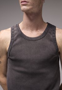 Σκούρο γκρι ριμπ αμάνικο τοπ με στρογγυλή λαιμόκοψη και φαρδιές μασχάλες· διαθέτει λεία υφή και ενισχυμένες ραφές.