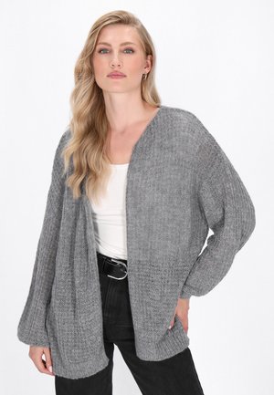 Cardigan gri tricotat cu deschidere în față, material texturat, mâneci lungi și tiv rib traditional. Purtați peste un top alb și completat cu pantaloni negri.