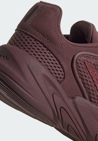 Körsbärsröd sportskor med ovandel i mesh och mockadetaljer, en strukturerad mellansula och en slät gummisula med synliga mönster.