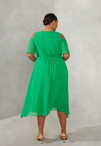 Grön, knälång klänning i flödande, lätt tyg. Har korta ärmar med utskärningar på axlarna och elastisk midja.