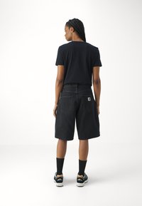 Svart bomull t-skjorte med korte ermer, parret med knelengde svarte denimshorts. Svarte joggesko med hvite såler og svarte sokker fullfører antrekket.