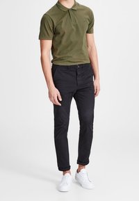 Olivově zelené polo tričko s krátkým rukávem a límečkem, kombinované s černými skinny kalhotami a bílými teniskami. Jednoduchý design bez vzorů.