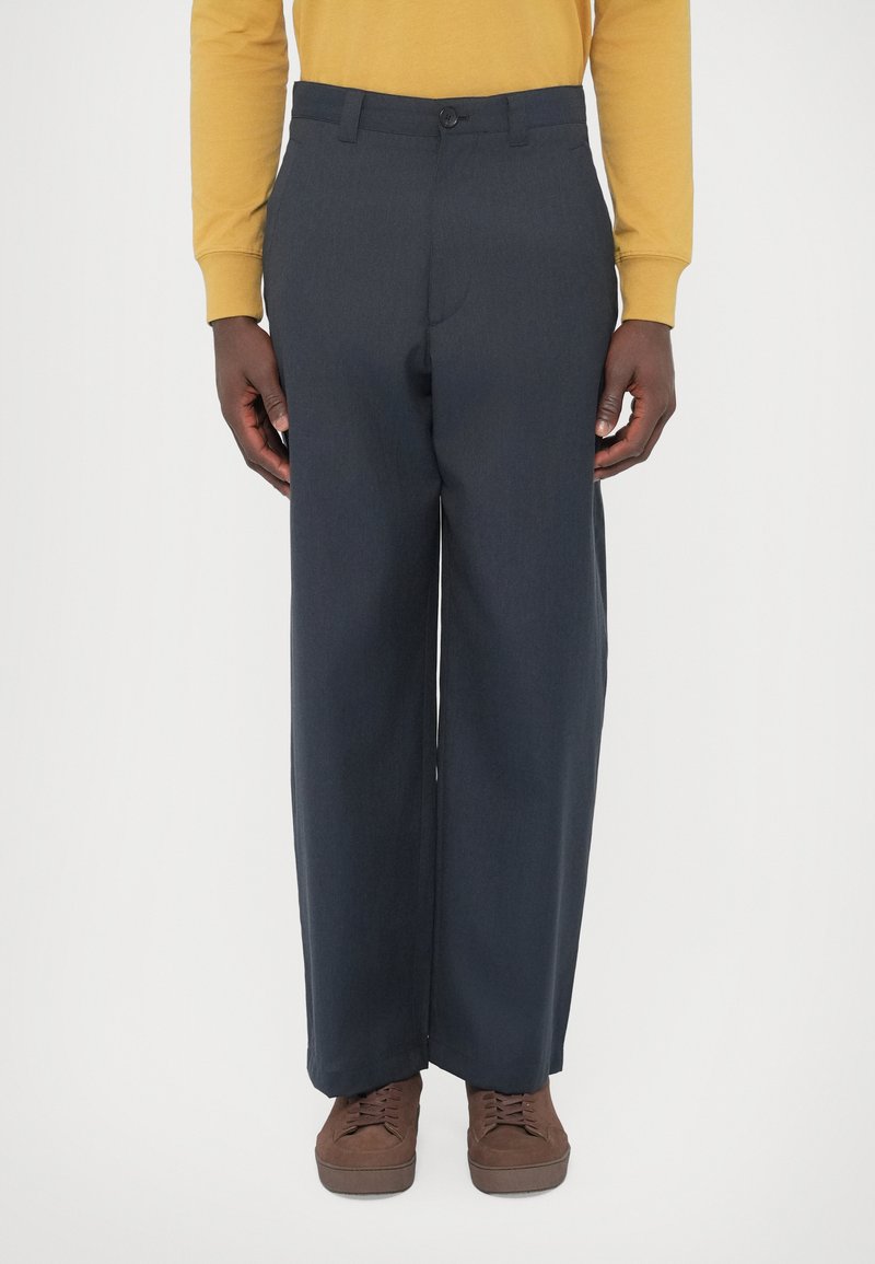 Pantaloni su misura blu navy realizzati in tessuto morbido, con chiusura a bottone, gambe dritte e una texture liscia. Indossati con scarpe marroni.