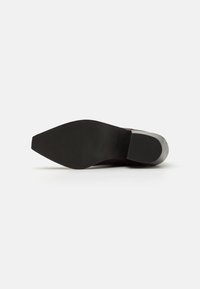 Semelle de chaussure noire avec une surface texturée et un bout légèrement pointu. Présente un petit talon et des bords lisses.