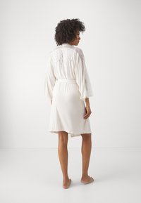 Robe bianca con maniche in pizzo e ricamo "Sposa" sul retro. Il tessuto è morbido, con un taglio a lunghezza ginocchio e una vita legata.