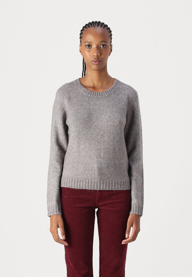 Suéter gris acogedor de punto suave con un cuello redondo de canalé y dobladillo. Combinado con pantalones de pana burdeos, que presentan un ajuste relajado.