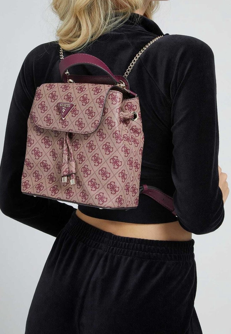 Lille burgunderfarvet rygsæk med mønster lavet af tekstureret stof, har et topgreb, justerbare stropper og metal accenter på hardware.