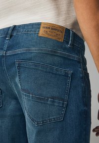 Denim jeans in een donkerblauwe wassing met een gestructureerde afwerking. Beschikt over een leren label op de tailleband en twee achterzakken met zichtbare stiksels.
