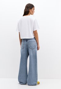 Un tricou alb scurt cu mâneci scurte, asortat cu blugi largi de culoare albastru deschis, având două buzunare pe spate și o textură de denim decolorat.
