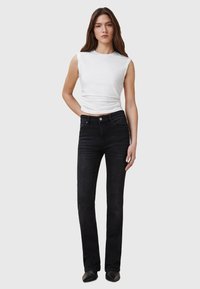 Jeans neri a campana con cinque tasche, vita aderente e sbiaditure delicate. Abbinati a un top bianco senza maniche aderente.
