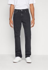 Vaqueros de mezclilla de lavado oscuro con un corte recto, diseño de cinco bolsillos y cierre de botón metálico. Combinados con una camiseta blanca básica y zapatillas blancas.