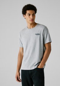 Camiseta de algodón gris con cuello redondo y mangas cortas, con el logo de "Red Bull Racing" en azul marino en el lado izquierdo del pecho.