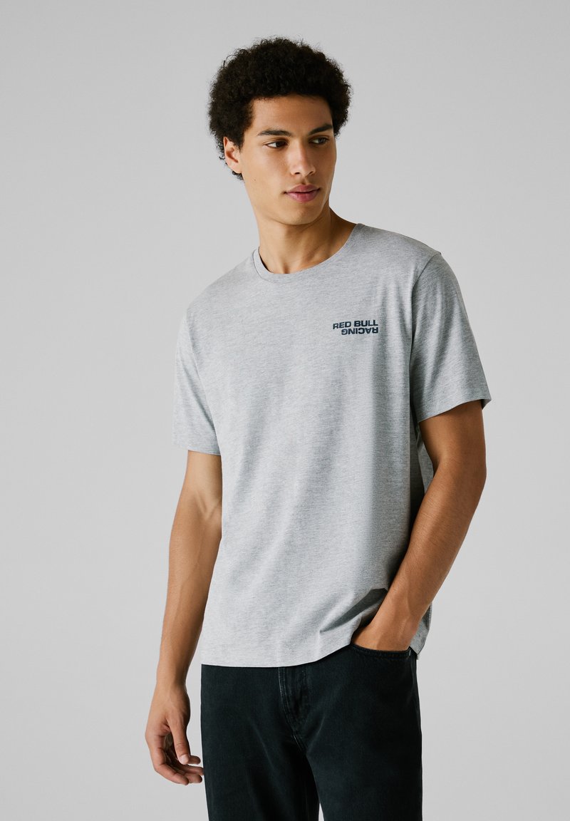 Camiseta de algodón gris con cuello redondo y mangas cortas, con el logo de "Red Bull Racing" en azul marino en el lado izquierdo del pecho.