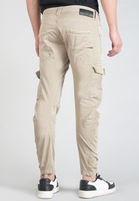 Beige cargobroek met zijzakken, taps toelopende pijpen en elastische boorden. Gemaakt van lichtgewicht stof, voorzien van een leren label op de achterkant.