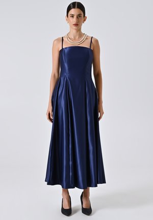 Abito da sera in satin blu navy con scollo aderente, spalline sottili e gonna svasata. Nota per la sua consistenza liscia e la silhouette elegante.
