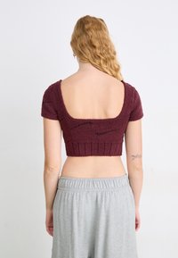 Sweater cropped bordeaux com mangas curtas, tecido texturizado, costas em forma de barco largas e bainha canelada. Combinado com calças cinzas de corte solto.