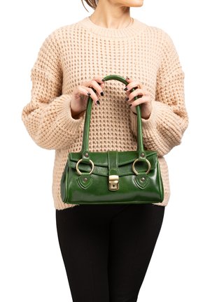 Grüne Lederhandtasche mit glatter Textur, doppelten runden Griffen, Klappe auf der Vorderseite und goldenen Hardware-Akzenten. Getragen mit einem cremefarbenen Pullover.
