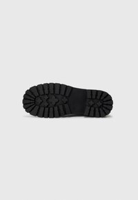 Suela de zapato de goma negra con surcos profundos y un patrón en cruz. Estructurada para tracción, con una textura sólida y duradera.