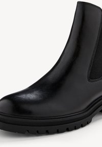 Botín Chelsea de cuero negro con un acabado suave, paneles laterales elásticos, puntera redondeada y suela resistente con patrones de textura.