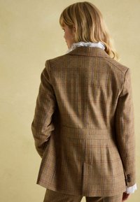 Hnedý károvaný blejzer s priliehavým strihom, s jemnými modrými a hrdzavými akcentami, štruktúrovanou tkaninou, jedným zadným rozventilovaním a gombíkovými manžetami.
