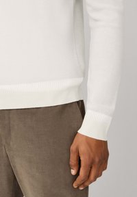 Maglione a maglia bianco con un motivo testurizzato, caratterizzato da polsini e vita a coste, abbinato a pantaloni in corduroy marrone.