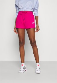 Rosa Nike-shorts med dragsko i midjan, med en vit logotyp. Matcher med vita och grå sneakers med röda accenter och ankelsockor.