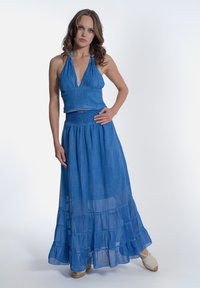 Top corto blu a halter abbinato a una gonna lunga a strati in un tessuto leggero e semi-trasparente. La gonna presenta una vita arricciata e un orlo a volants.