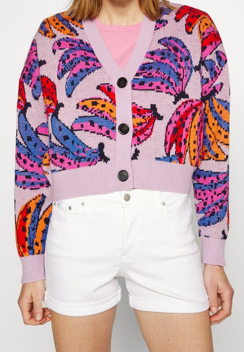 Strikket cardigan med en lilla bundfarve og et livligt bananmønster i rød, pink, orange og blå, fem sorte knapper og ribstrikkede ærmekanter.