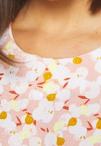 Tissu de robe à fleurs avec un fond rose présentant des fleurs blanches et jaunes, rehaussé de petites feuilles rouges, surface texturée.