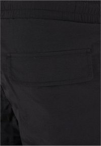 Gros plan sur un tissu noir avec une poche rectangulaire cousue et un détail de ceinture élastique.