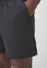 Schwarze Sportshorts aus weichem Stoff, mit einem Elastikbund und seitlichen Taschen. Auf der Vorderseite befindet sich ein kleines schwarzes Nike-Logo.