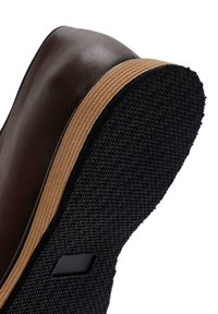 Scarpa di pelle marrone con punta rotonda, dotata di una suola in gomma nera testurizzata e di una striscia a metà suola beige. Nessun hardware o accento degno di nota.