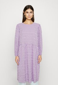 Vestido de mangas longas em lilás claro com bolinhas pretas, apresentando uma saia franzida e decote redondo, feito de um tecido leve.
