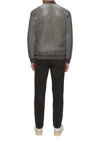 Grau Bomberjacke mit glatter Textur, gerippten Bündchen und Saum, über schwarzen Jeans und weißen Sneakers getragen, von hinten gezeigt.