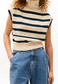 Sweter dziany z wysokim kołnierzem, w kremowo-granatowe poziome paski, z krótkimi rękawami i żebrowanym pasem; zestawiony z niebieskimi dżinsami.