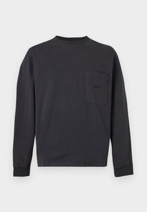Jeune homme face à l'avant portant une chemise noire à manches longues avec une poche poitrine et un jean noir déchiré avec un motif clouté sur une jambe.