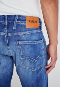 Jeans in denim blu con un'etichetta in pelle REPLAY, cuciture a contrasto e design ricamati sulle tasche con una leggera texture usurata.