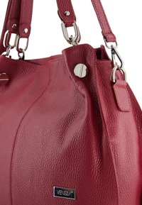 Red textured leather handbag with silver hardware, featuring dual straps and an embossed logo plate. Smooth and durable material.