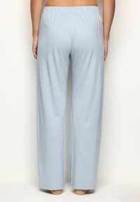 Persona vestida con pantalones de lounge sueltos de color azul claro y cinturilla elástica, de pie descalza frente a un fondo blanco liso.