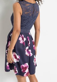 Námořnické květinové šaty s krajkovým korzetem, bezrukávovým designem a rozšířenou sukní s růžovými a bílými květinovými vzory. Detail s knoflíky na zadní straně.