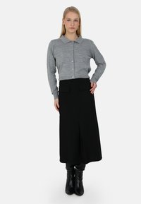 Harmaa napillinen neuletakki, jossa on pieniä koristeita, yhdistetty mustiin hameeseen, jossa on etutaskut, ja käytössä polven mittaiset mustat saappaat.