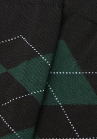 Detailní záběr na pletenou látku s černým a tmavozeleným diamantovým vzorem, protnutým tenkými bílými šitými diagonálními linkami.