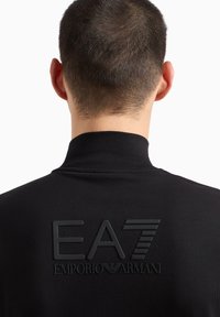 Felpa nera con colletto alto caratterizzata da un logo EA7 testurizzato e "EMPORIO ARMANI" in rilievo sul retro. Tessuto morbido con un design aderente.