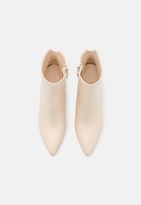 Bottines beige à bout pointu avec boucles latérales, vues de dessus sur un fond blanc uni.