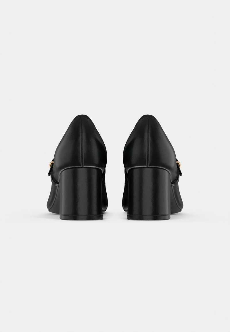 Paire de chaussures noires en cuir à talon bloc vues de dos, avec un design épuré et un petit détail de boucle dorée sur les côtés.