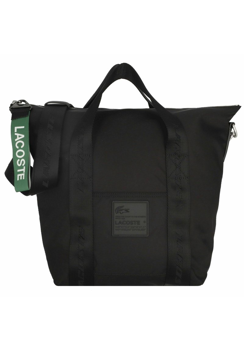Sac tote Lacoste noir avec double poignées, fermeture éclair et bandoulière verte arborant le logo Lacoste blanc.