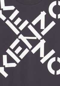 Černá mikina s kulatým výstřihem, která má výrazný bílý text uspořádaný diagonálně. Materiál vypadá měkce s mírným leskem, což zdůrazňuje grafický design.