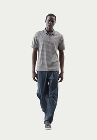 Polo a maniche corte da uomo con motivo geometrico in bianco e nero, abbinato a pantaloni larghi blu navy e sneakers grigie.