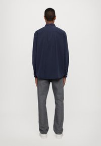 Navyblauw overhemd met lange mouwen, verticale strepen, kraag met knopen en één knoop aan de achterkant, gecombineerd met grijze rechttoe rechtaan jeans en witte sneakers.
