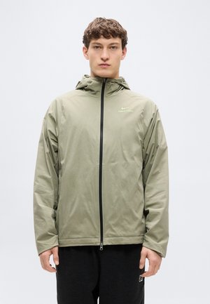 Letvægts olivengrøn lynlåstrøje i glat stof med hætte, sort lynlås og diskret logo på brystet.